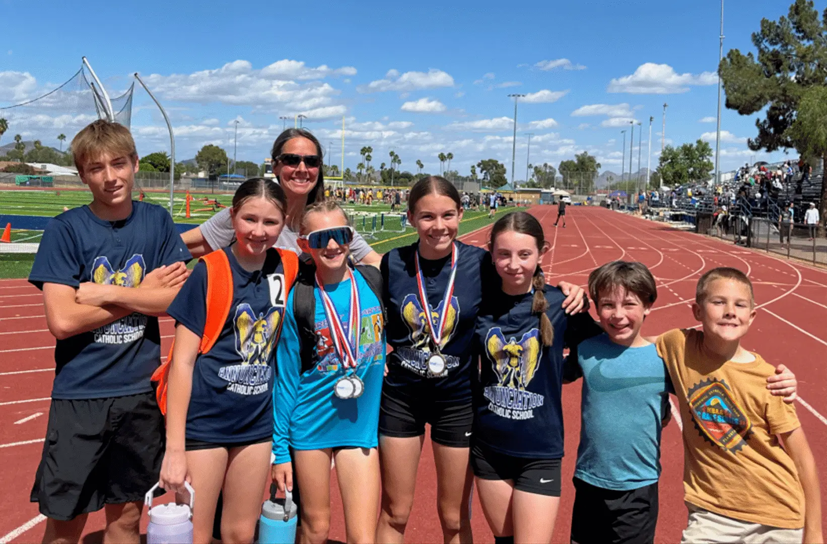 Five young athletes posing with medals on a sunny track field.