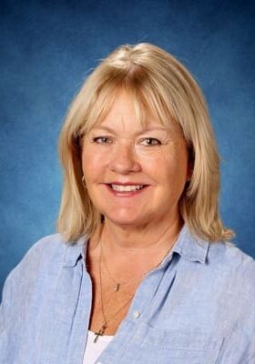 A smiling blonde woman in a light blue shirt against a blue background.