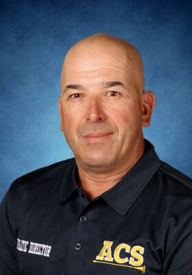 Portrait of a bald man in a dark uniform against a blue background.